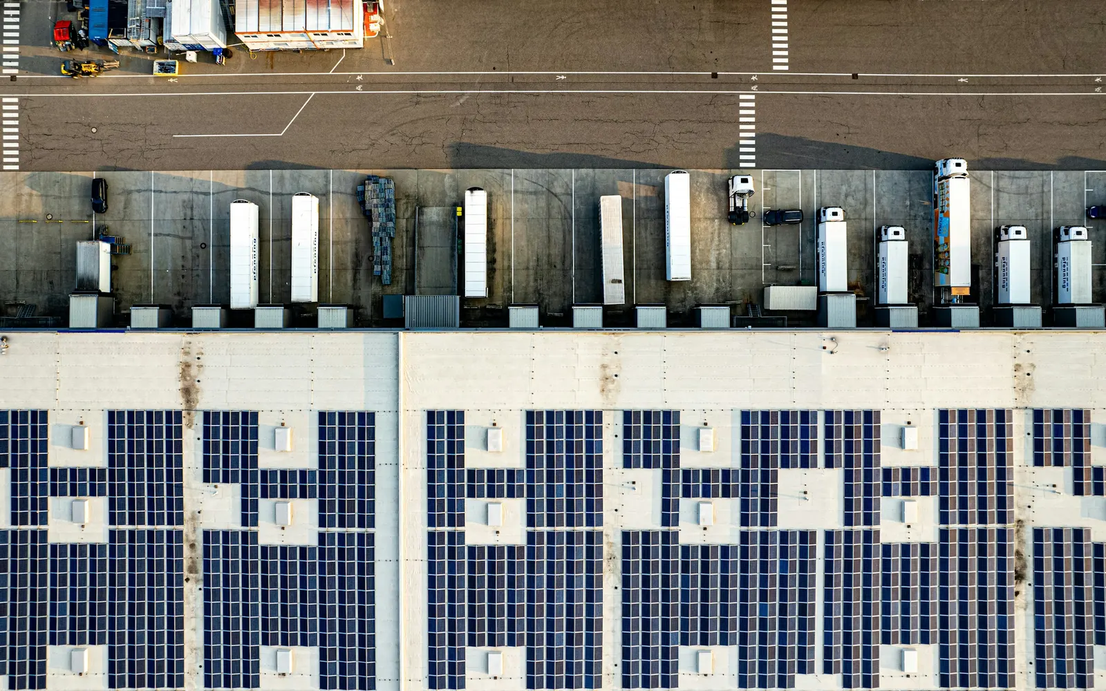 Luftaufnahme eines Logistikgebäudes mit Photovoltaikdach, Laderampen und Lastwagen